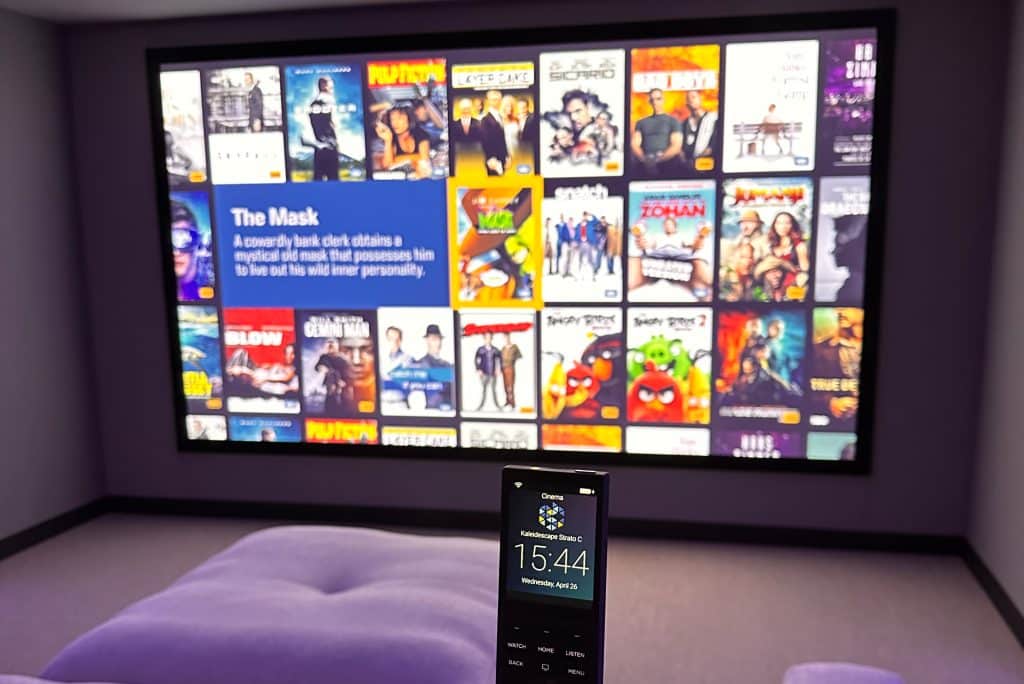 A home theatre setup with a large projector screen displaying a grid of film posters, including The Mask. A person is holding a remote control, and the time on its display reads 15:44. | Ibiza